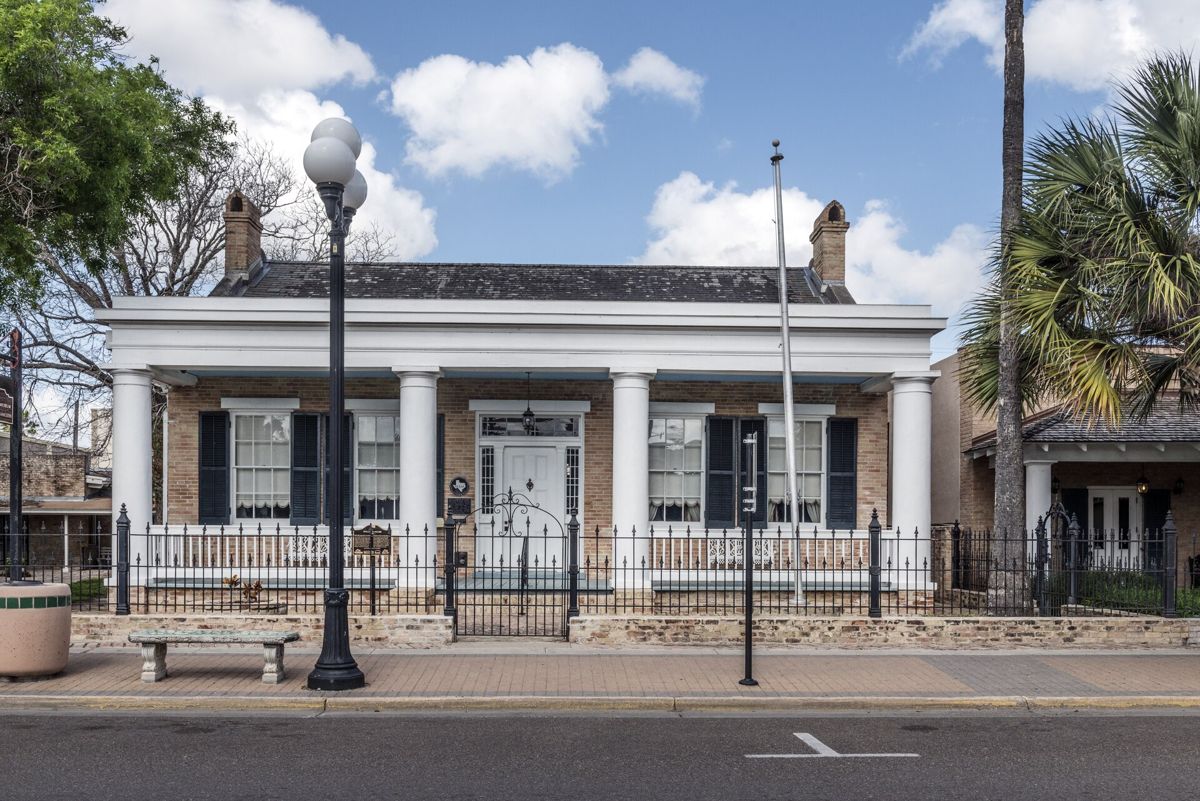 The Stillman House Museum in downtown Brownsville, Texas, a one-story brick house with a white columned porch under a blue sky